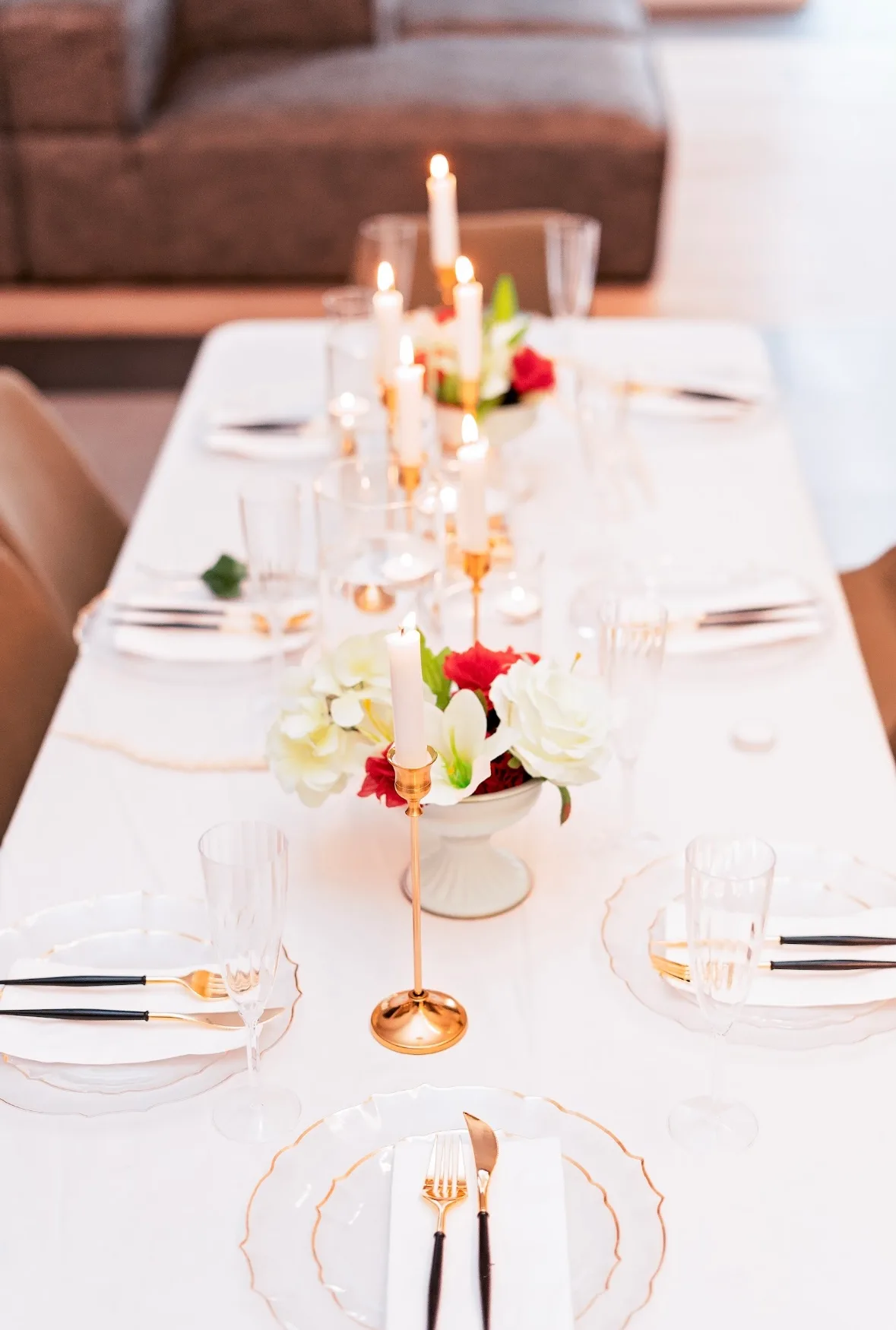 A white event table set with gold candle holders, clear vessels and floral details